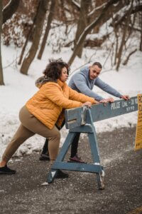 focused black couple warming up near wooden barrier in forest