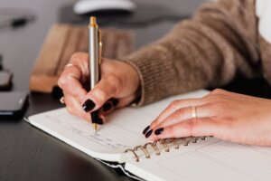 crop woman writing down notes in diary