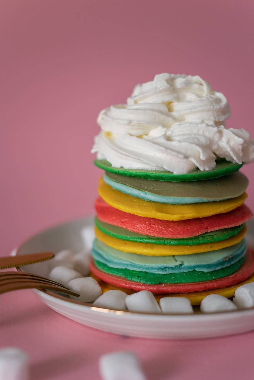 colorful pancakes topped with whipped cream against pink background