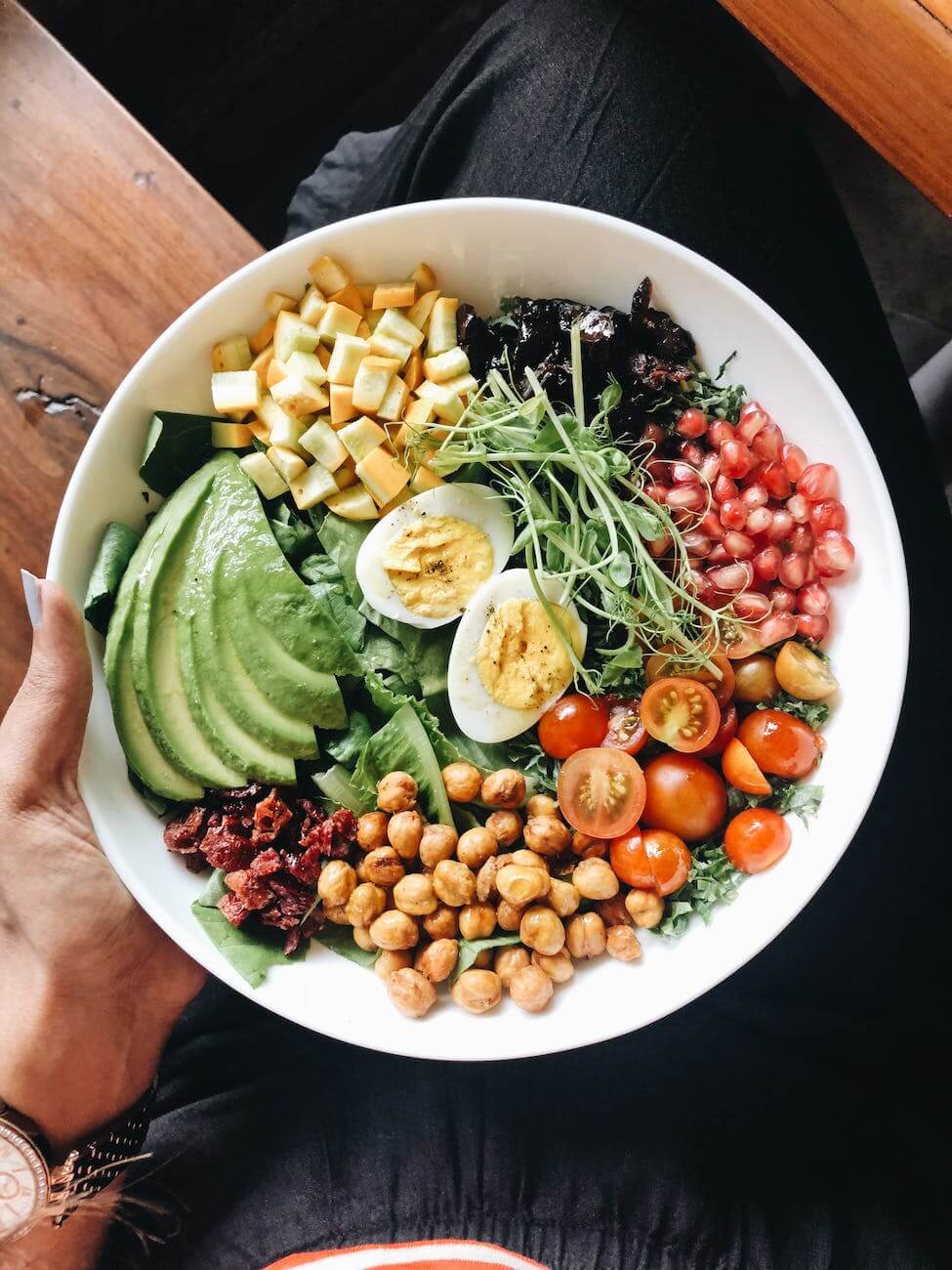 a hand holding a white ceramic bowl with fresh salad