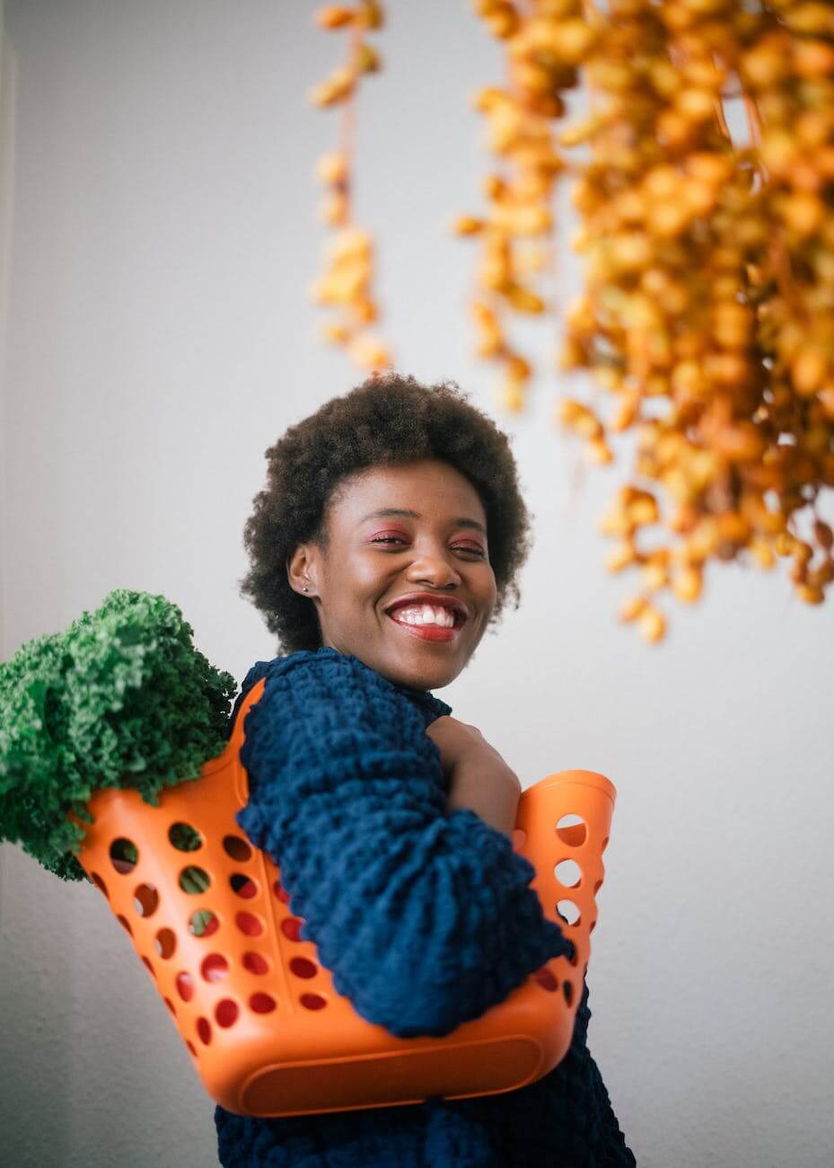 happy young black woman holding basket with lettuce on shoulder adopting a healthy lifestyle