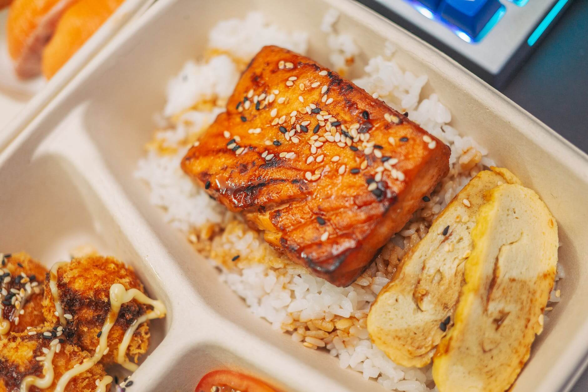 a rice topping of roasted salmon with sesame seeds and scrambled egg in a take out container