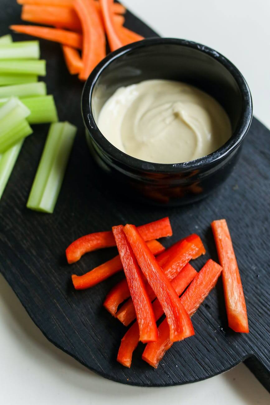 fresh sliced vegetables served with sauce in black bowl on tray as balanced snacks