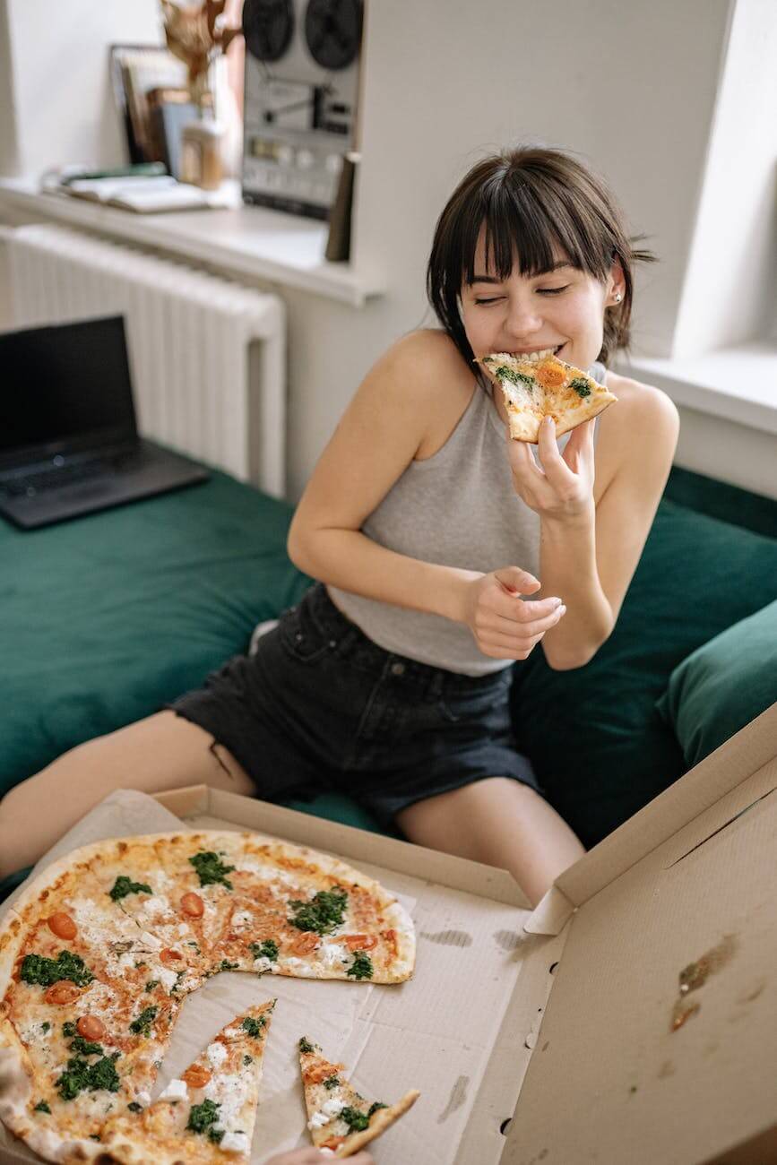 woman in gray tank top eating pizza