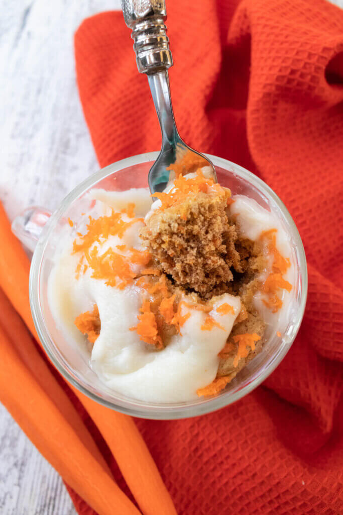 Carrot cake mug cake on orange kitchen towel with cream cheese frosting