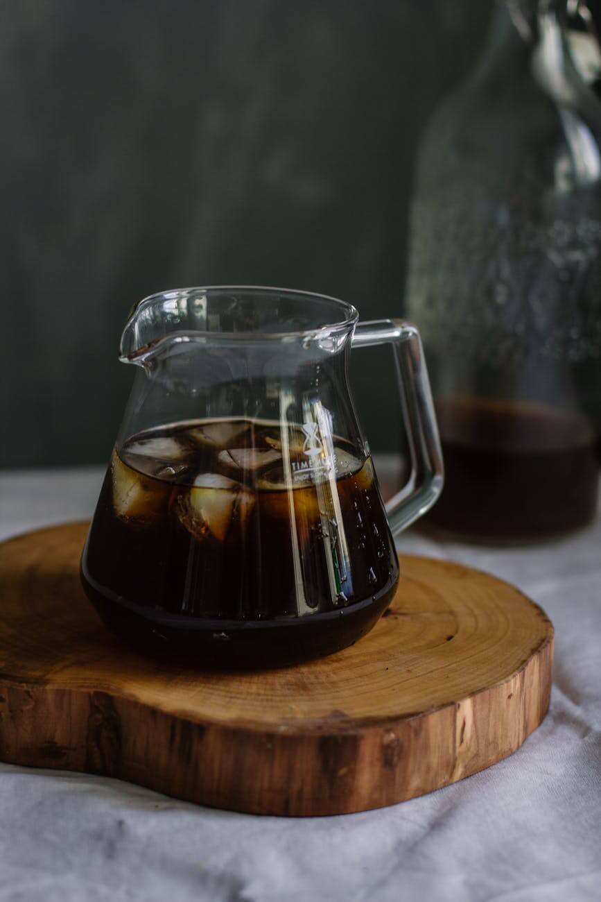 clear glass pitcher with cola and ice on wooden chopping board